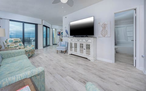 Relax in the inviting living area featuring a large TV, comfortable seating, and beachfront balcony views