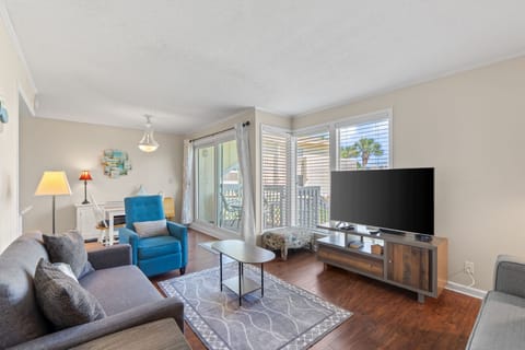 Settle into your inviting living room with coastal touches, where natural light floods through patio doors and your private balcony awaits with palm-fringed views.
