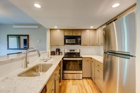 Modern kitchen with stainless steel appliances, marble countertops, and wooden cabinets. The space is well-lit with recessed lighting and features a sink with a gooseneck faucet in an island.