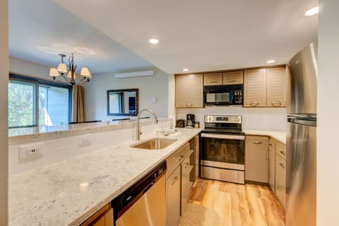 Modern kitchen with stainless steel appliances, beige cabinets, and a light granite countertop. A double sink and a dishwasher are built into the island. A chandelier hangs near the sliding glass door.