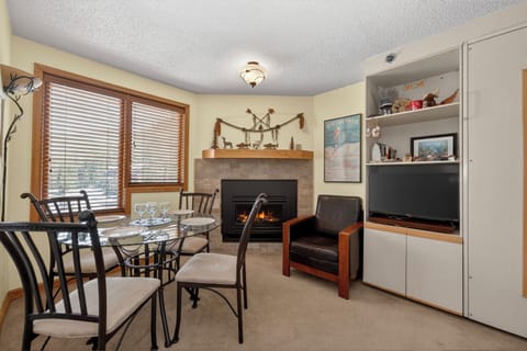 Gather around the dining table or cozy up by the fireplace in this inviting space. Natural light streams through large windows, while the warmth of the fire and mountain-themed décor create your perfect retreat.