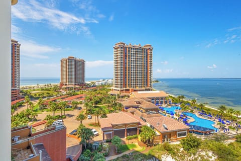 Aerial view of the beachfront property featuring resort towers, tropical landscaping, a winding pool complex, and direct access to sandy shores along the sparkling coastline.