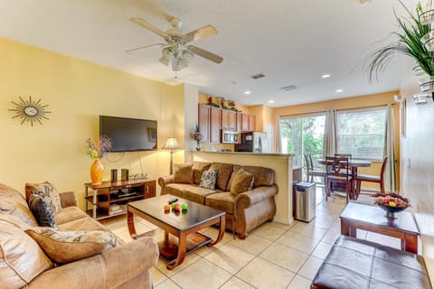 Sunlight filters through large windows over the tiled living room with brown suede sofas and a wooden coffee table.