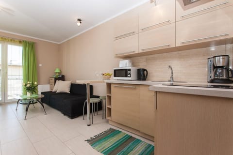 A view of the kitchen and dining area, with a small dining table for two and bright green curtains hanging by the large window, which brings in plenty of natural light.