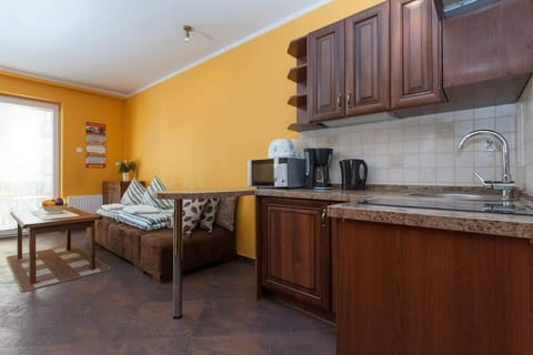  A view of the kitchen area with dark wooden cabinets and appliances like a kettle and coffee maker. A small dining table and two chairs are placed by the kitchen.