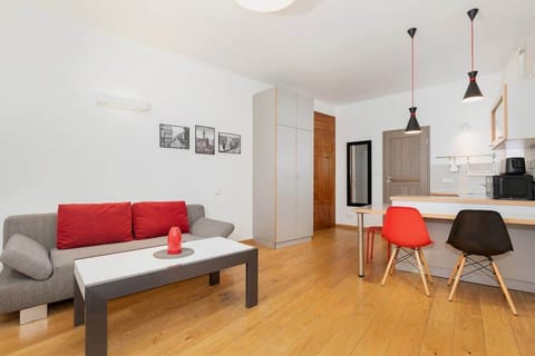 A cozy living room featuring a modern red sofa and a small coffee table. The room has light-colored wooden floors and is decorated with simple black-and-white artwork on the walls.