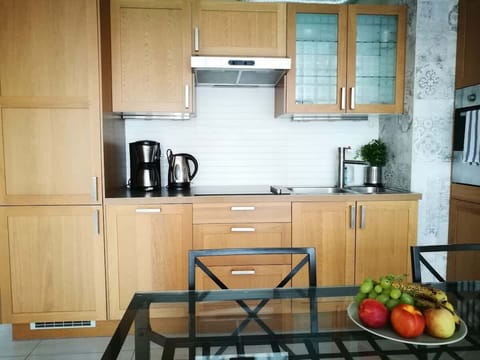 A compact kitchen featuring light wood cabinets, a black countertop, and a small dining area with fruit on display, adding a splash of color.