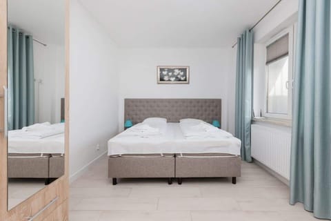 This room features a queen-sized bed with light bedding. Large windows allow ample natural light to fill the room, and the light-colored walls contribute to a fresh, airy atmosphere.