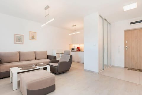 Brown and beige living room with white kitchenette, television, and coffee table.