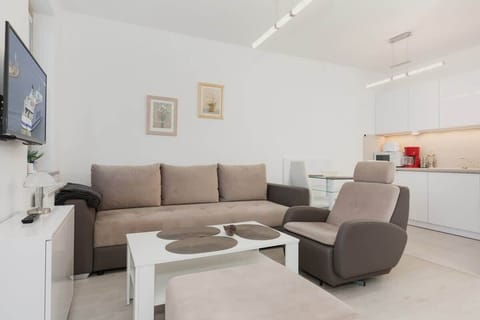 Cosy and elegant living room with stylish sofa bed, armchair, television, and white kitchenette.