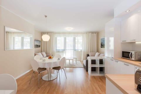 An open-plan living room with a kitchenette. The sofa is light-colored, and the room has a modern, minimalistic design with wooden floors and sleek furniture.