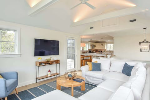 living room with vaulted ceilings and exposed beams, wall mounted TV, looking into kitchen