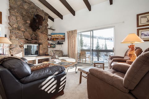 Cozy up in this rustic living room with stone fireplace and stunning ski slope views through your private balcony.