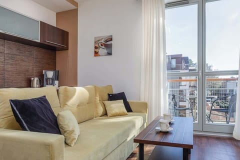 A living room with access to the balcony, featuring cream-colored seating and accent cushions, providing a cozy and airy atmosphere.