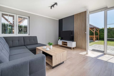 A bright, modern living room featuring a gray sofa, a light wooden coffee table, and large windows that let in plenty of natural light, with a garden view in the background.