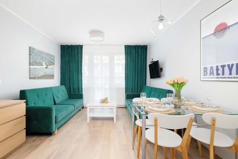 A modern living room featuring a green sofa, a dining table with chairs, and large windows with green curtains.