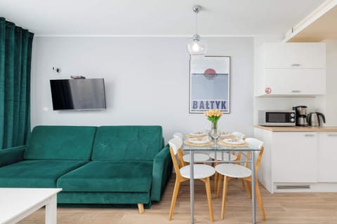 A bright space with a green sofa, dining table, and artwork on the walls, complemented by white furnishings.