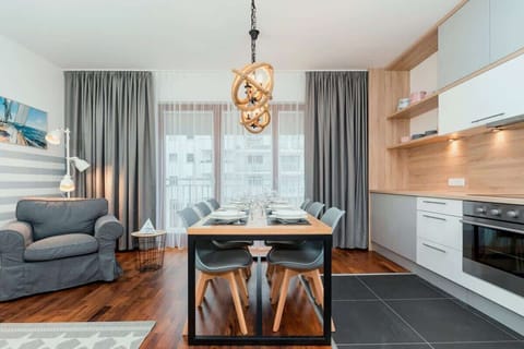 The living room from a different perspective showing a large table for 6 people. A disagner lamp hangs above the table.  To the right is the kitchenette matching the design of the entire room. 