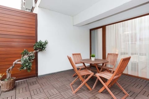 A spacious balcony with wooden flooring, outdoor furniture, and a green plant.

