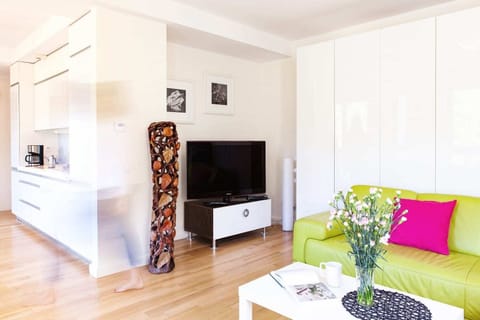 Another angle of the living room showing a white console and green sofa with pink and purple pillows. A modern, minimalist aesthetic is enhanced by colorful decor and soft lighting.