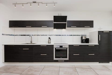 A sleek kitchen with dark cabinetry, a tiled backsplash, and modern appliances.