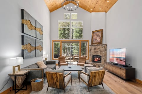 Relax in this inviting living room with soaring vaulted wood ceilings, cozy stone fireplace, and stunning views through floor-to-ceiling windows that frame the surrounding forest.