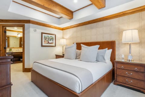 Bedroom with leather-upholstered bed, patterned accent wall, wooden nightstands, and lamps under exposed wood beams.