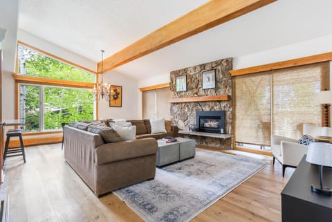 Vaulted ceiling with exposed wooden beam and large windows overlooking lush greenery in the living area.