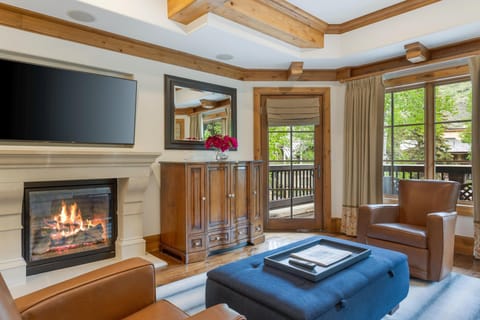 Living room with leather armchairs, blue tufted ottoman, stone fireplace, and glass door leading to balcony.
