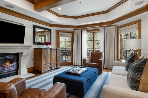 Living room features leather armchairs, a blue upholstered ottoman, and a fireplace beneath a wall-mounted TV.