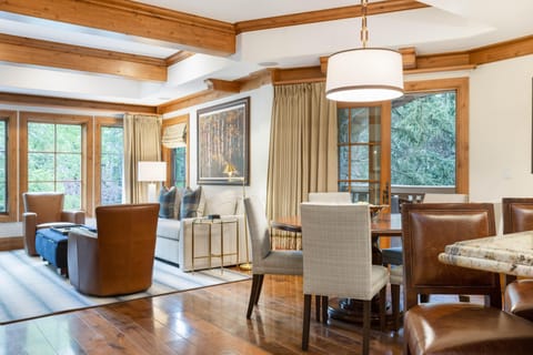 Leather armchairs and a white sofa with plaid pillows surround a blue ottoman in the living area with wood beams overhead.