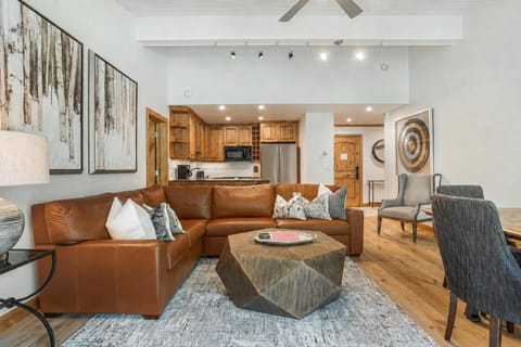 Top-floor living area with vaulted white ceiling, geometric wood coffee table, brown leather sectional sleeper sofa, and pine floors.