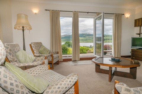 Full height windows with door to patio, seating and views of Loch Awe and garden