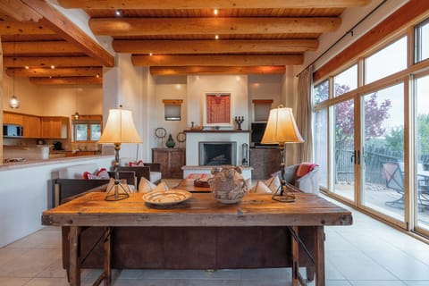 Relax in your spacious living area featuring stunning exposed beam ceilings, a cozy fireplace, and warm natural light flooding through floor-to-ceiling windows overlooking the outdoor terrace.