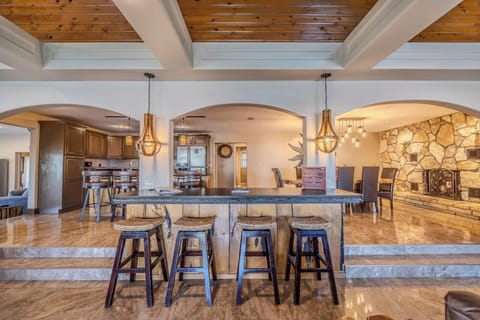 "Spacious kitchen and bar area with stylish lighting and stone fireplace view."