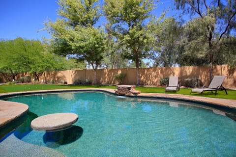 Resort-style pool with waterfall feature, putting green, and shaded lounging in a fully private yard.