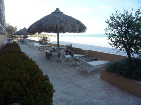 Beachfront patio with lounges, tables with tiki huts for some shade.