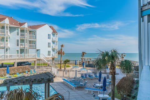 A luxurious resort with a sparkling pool overlooking the ocean, surrounded by lush greenery and palm trees, set against a backdrop of Gulf of Mexico.