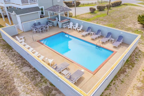 Aerial view of the property's private swimming pool area, surrounded by sun loungers and an outdoor dining space, positioned in a coastal neighborhood with nearby green spaces.