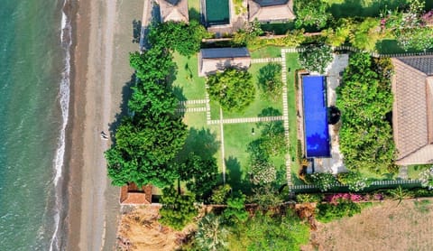 Aerial view showing the villa, garden, pool, and direct beach frontage. 