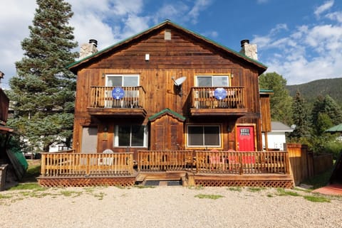 A charming wooden mountain lodge with spacious balconies, surrounded by evergreen forests and a bright blue sky—a welcoming retreat nestled in a serene mountain community.