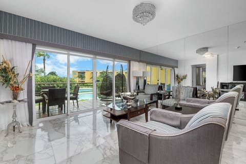 Elegant living space with sparkling chandelier, plush seating, and polished marble floors. Glass doors lead to a private terrace overlooking the pool—ideal for morning coffee or evening relaxation.