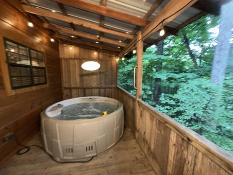 Enclosed wooden porch features a bubbling hot tub, string lights, and screened views of green forest trees.