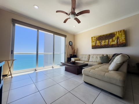 Sectional sofa in cream leather faces a dark wood coffee table, with sliding glass doors revealing ocean views.