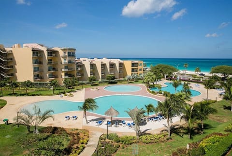 Beachfront resort property features sparkling pools surrounded by tropical gardens, with direct access to the turquoise ocean and sandy shores.