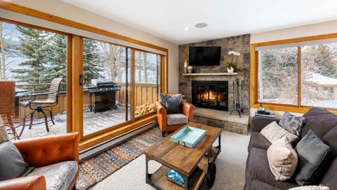 Step into your cozy retreat with a stunning stone fireplace, plush seating, and floor-to-ceiling windows framing snowy mountain views—perfect for unwinding after a day on the slopes.