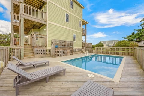 The exterior view shows a multi-level beach house with private pool deck surrounded by coastal greenery and neighboring properties—a welcoming arrival feature.