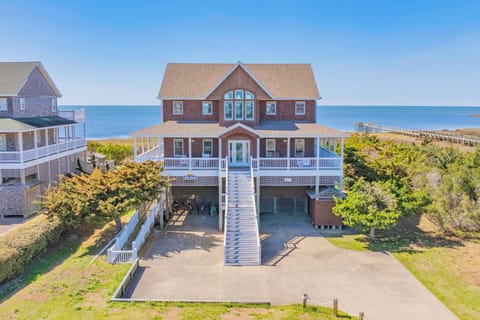 Beachfront property featuring classic coastal architecture with wraparound porches and elevated design, steps from ocean access and surrounded by natural dunes.