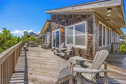Weathered cedar shingles and Adirondack chairs lining a spacious deck under a clear blue sky invite you to unwind outdoors at this coastal retreat.