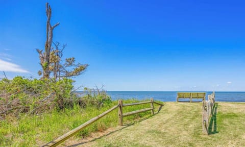 Coastal property path leading to a private waterfront access point overlooking calm sound waters, framed by natural grasses and weathered coastal trees.